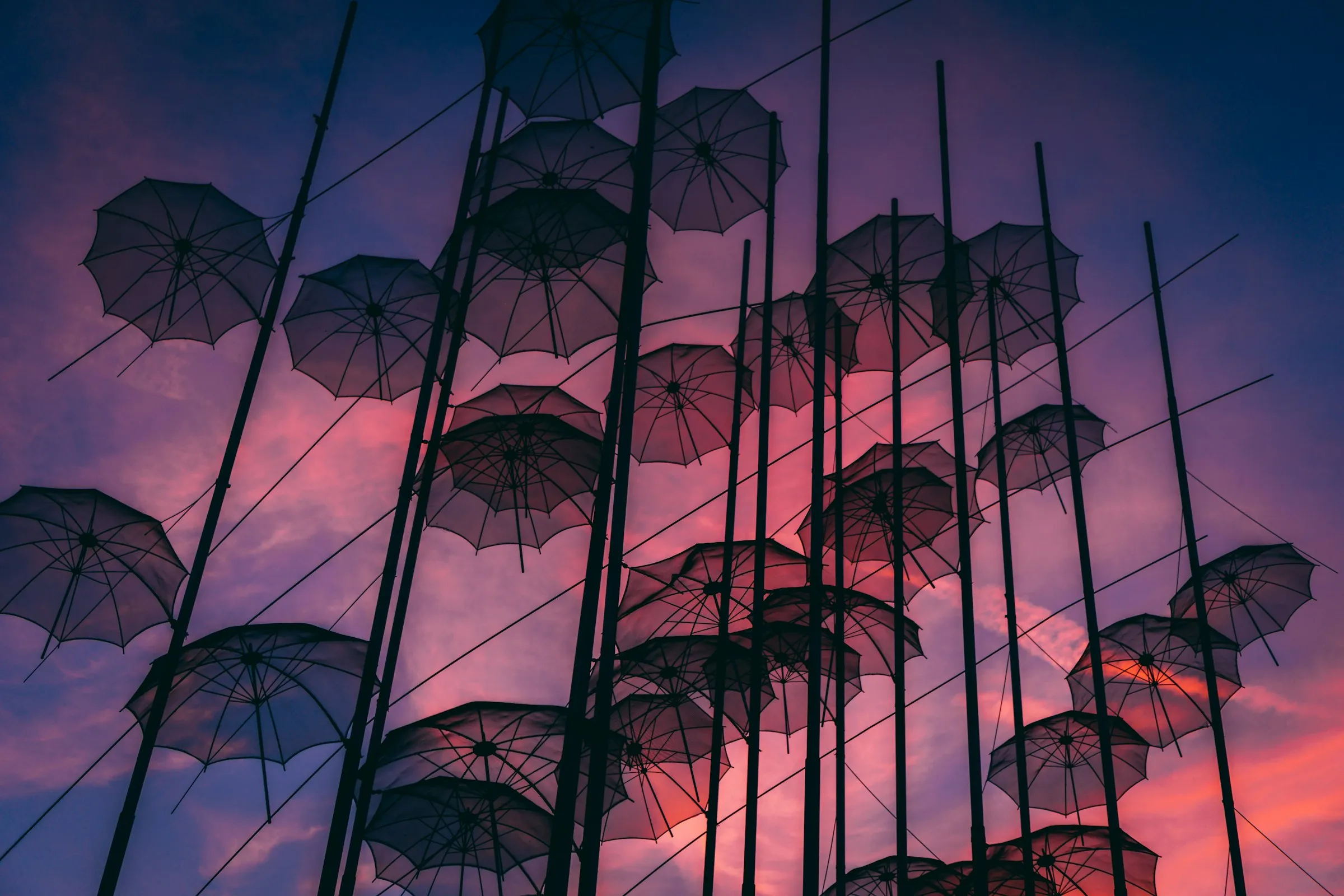 Umbrella sculpture silhouetted against a pink and purple sunset sky in Thessaloniki.